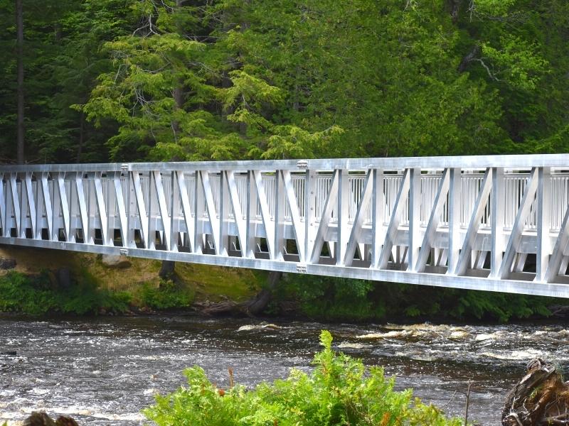 A bright chrome steel pedestrian bridge crosses the Tahquamenon River, providing access to Lower Tahquamenon Falls' river island for people of all abilities