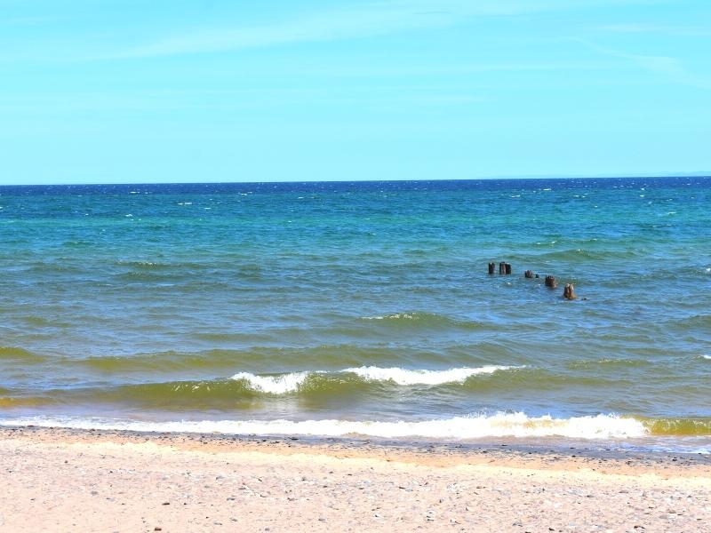 The many hues of blue on Lake Superior, with a pebbly beach in the foreground and some old wooden pylons peeking above the waterline.