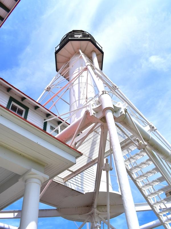 The Whitefish Point Light Station as viewed from the ground against a blue sky.