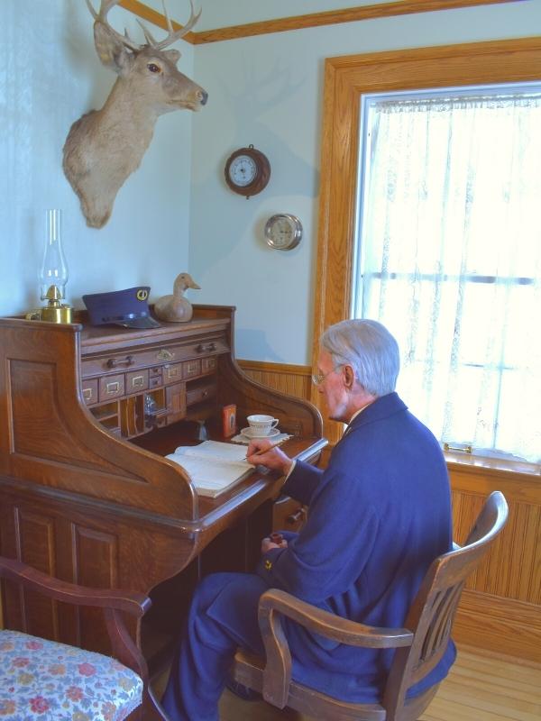 A realistic mannequin of a lightkeeper sits at a writing desk doing the accounts in the Lightkeepers Quarters at Whitefish Point