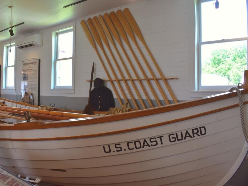 A large white row boat in a white building with wooden oars and a coast guard uniform on the wall