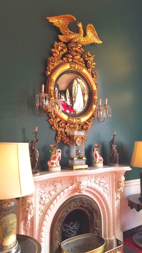 An ornate gold mirror with a decorative eagle, sitting atop a white stone carved fireplace at the Greenbrier