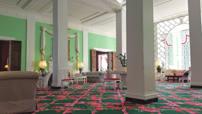 The Trellis lobby at the Greenbrier resort has luxurious lounge furniture, large white square columns, deep green and pink carpeting, and detailed molding on the ceilings