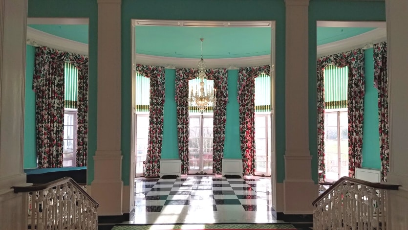 A teal terrace lobby at The Greenbrier resort with floral curtains and a black and white marble floor