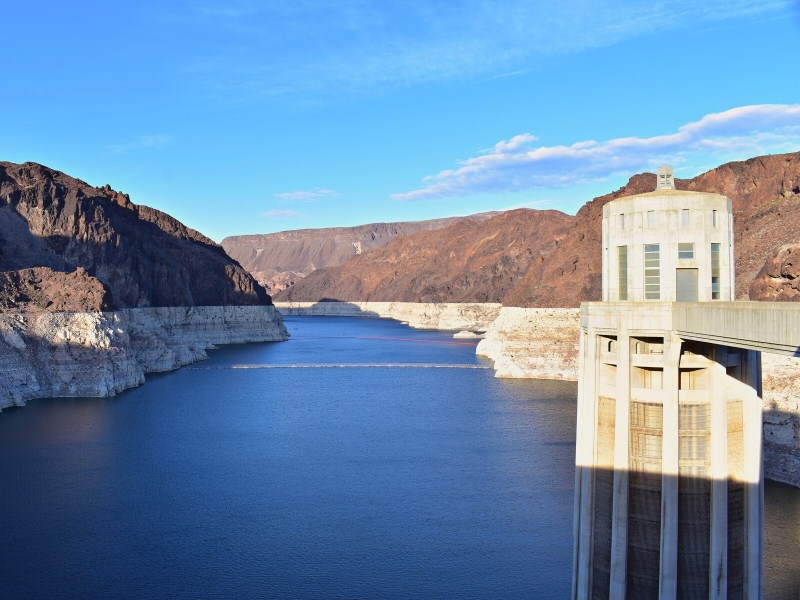 The dark blue waters of Lake Mead contrast with the white and red rock of the canyon walls, with a concrete intake tower in the foreground