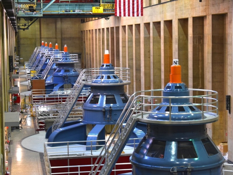 A row of generators with blue tops and orange tips line the inside of the Nevada power plant at Hoover Dam