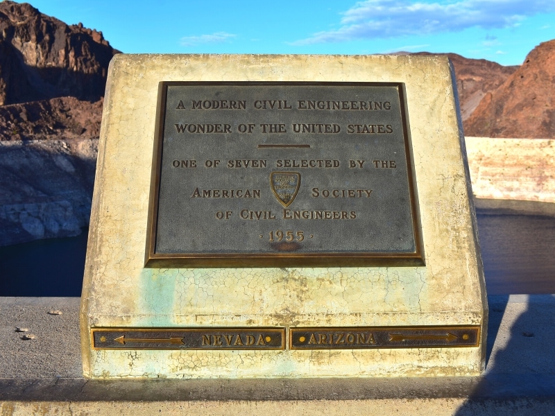 A metal plaque on stone base marks the state line atop of Hoover Dam and the significance of the Hoover Dam as one of the modern engineering marvels of the US.