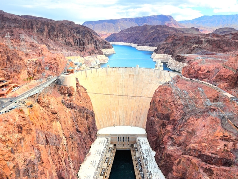 The large concrete face of Hoover Dam contains Lake Mead in the canyon to the rear and releases the Colorado River through the power plant below.
