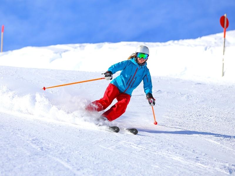 A skier in blue jacket and red pants stands out against the brilliant white snow of the ski slope