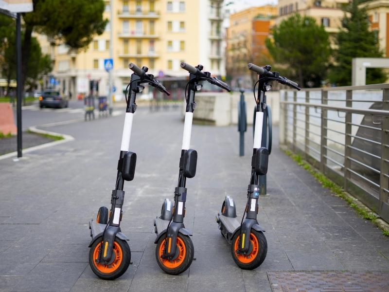 Three scooters parked in the middle of a sidewalk in an urban area.