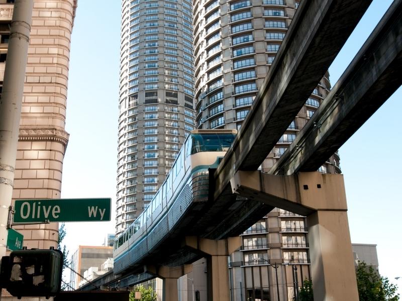 The Seattle monorail comes down its track in front of skyscrapers and Olive Way near Westlake Center.
