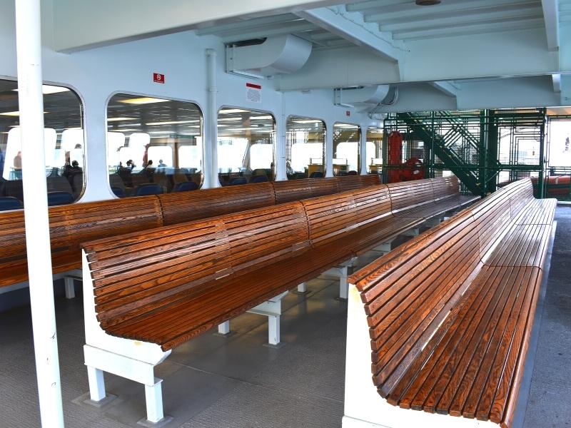 Three rows of long wooden benches bolted to the deck provide seating on an open-air deck of a ferry