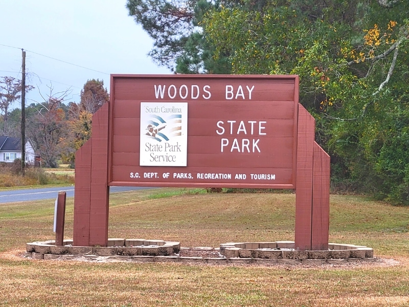 A large brown sign indicates the entrance to Woods Bay State Park in South Carolina