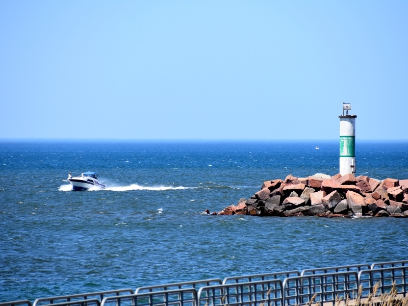 A small speed boat rounds the corner around a small lighthouse station on Lake Michigan at the Portage Lakefront and Riverwalk in Indiana Dunes National Park