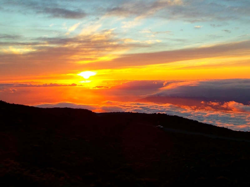 Sunset blurred behind clouds turns the sky red orange as seen from Haleakala's summit