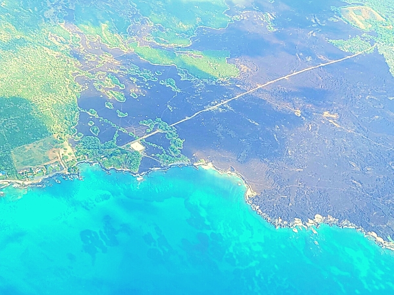 The southern shore of Maui as seen from an airplane, with vibrant greens contrasting old black lava flows and the blue hues of the ocean