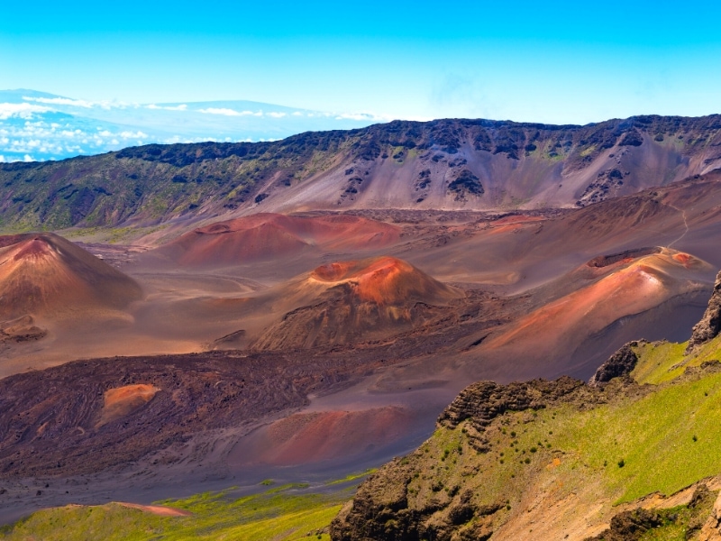 The inside crater of Haleakala is filled with smaller cinder cones with red, orange, and brown sand, while the ridgeline stays vibrant green.