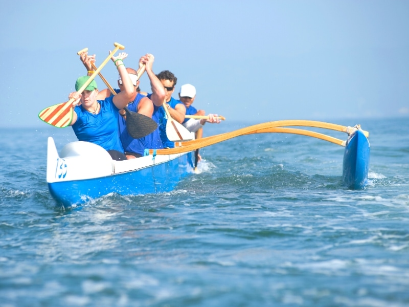 A team of 4 in blue paddle an outrigger canoe across the ocean