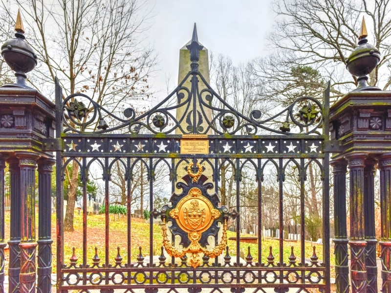 A detailed iron gate stands in front of the stone obelisk that marks Thomas Jefferson's grave in the cemetery at Monticello.