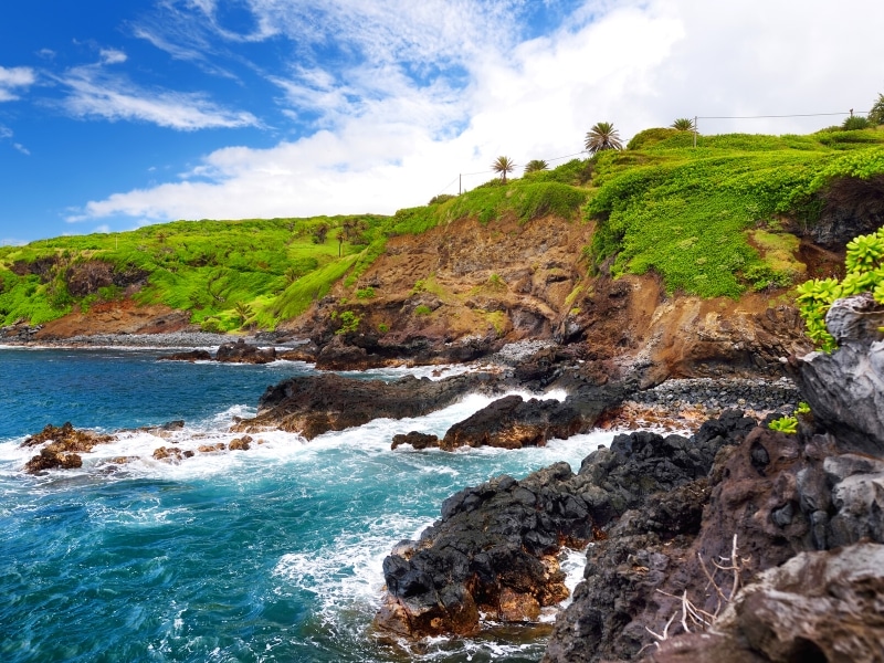 Rough, rocky coastline of Southern Maui with green grass and blue waters crashing on lava rocks