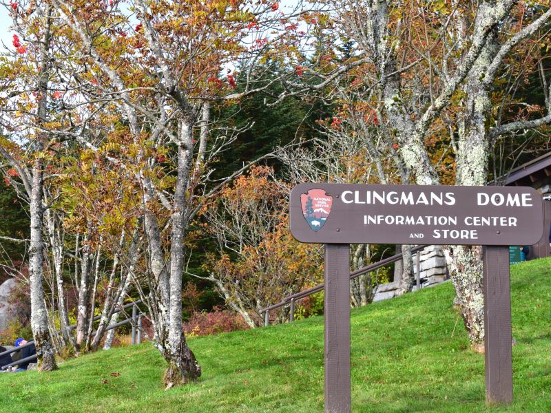 A simple brown signs indicates the Clingmans Dome Information Center and Store, built into the hillside and adorned with colorful trees