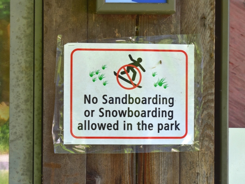 A simple sign showing a stick figure sandboarding with a red circle with a line through it, which says No sandboarding or snowboarding allowed in the park.