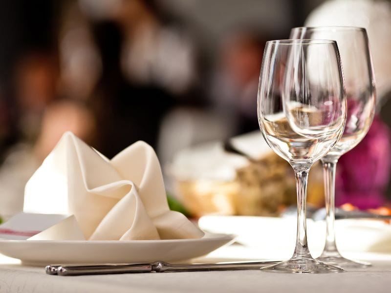 Empty wine glasses wait next to a place setting with a decoratively folded napkin atop the plate.