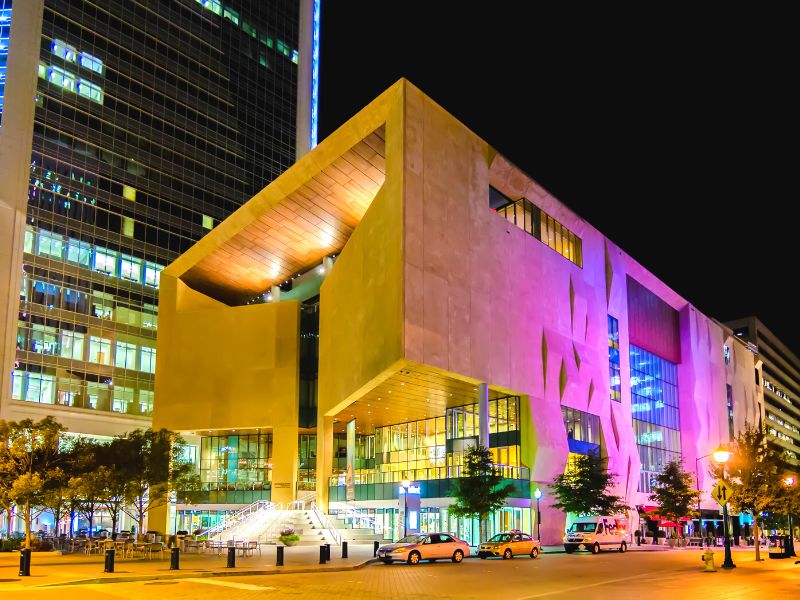 The Mint Museum Uptown location, lit up with yellow and purple lights at night.