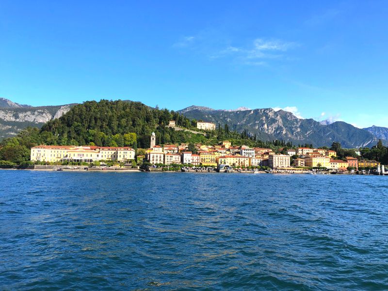 The town of Bellagio, Italy as seen from Lake Como, with colorful buildings on the waterfront and green trees atop the hillside