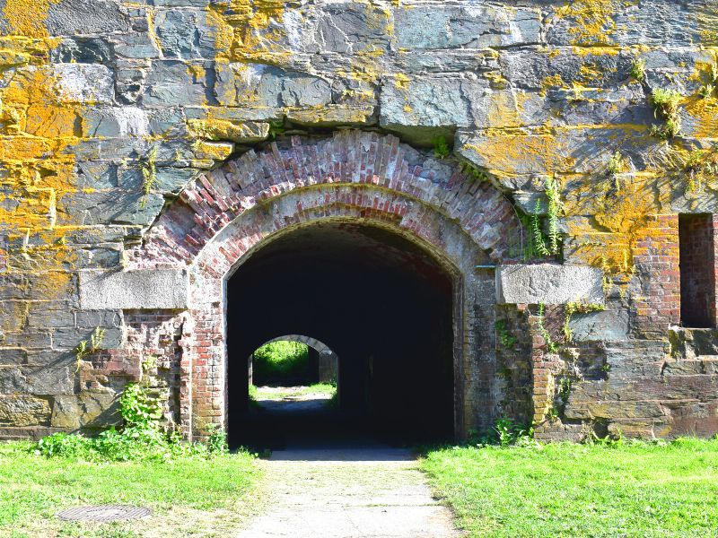 The stone fortifications of Fort Adams are covered in yellow moss as a brick tunnel dives into darkness beneath the wall