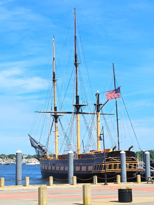 A replica colonial sailing ship, the Oliver Hazard Perry, sits at dock in Newport Harbor on a sunny day