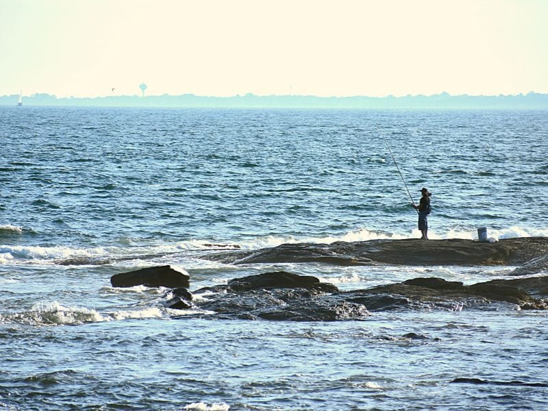 A lone fisherman on the rocks at Brenton Point overlooking the Atlantic Ocean on a hazy day