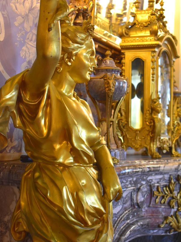 Close up of a golden statue and detailing around a pink marble fireplace in Marble House in Newport, RI