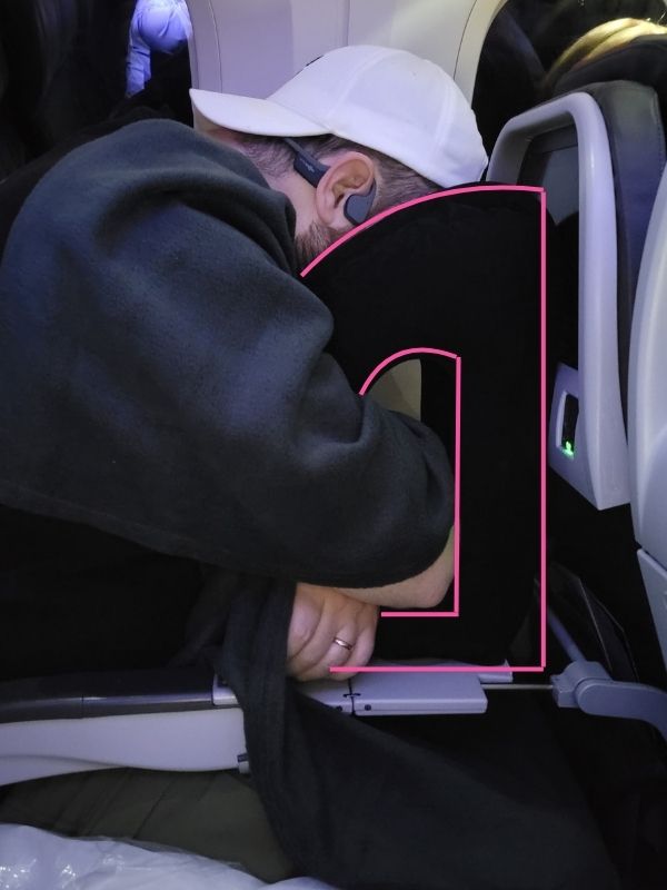 Man using an inflatable travel pillow, with pink outlines added to highlight the pillow